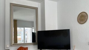 Et værelse med et stort spejl, et fladskærms-tv på et hvidt skab og en lille dekorativ genstand på væggen.