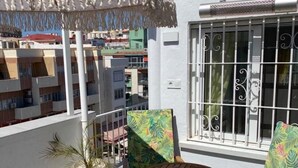 En balkon med et bord og stole, en potteplante og udsigt til omkringliggende bygninger.