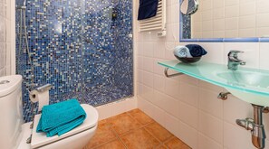 Bathroom features a shower, toilet, and sink with a glass shelf and terracotta floor.