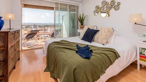 Relax in this serene bedroom with a large bed, nightstand, and potted plant, offering a view of the city from the balcony.