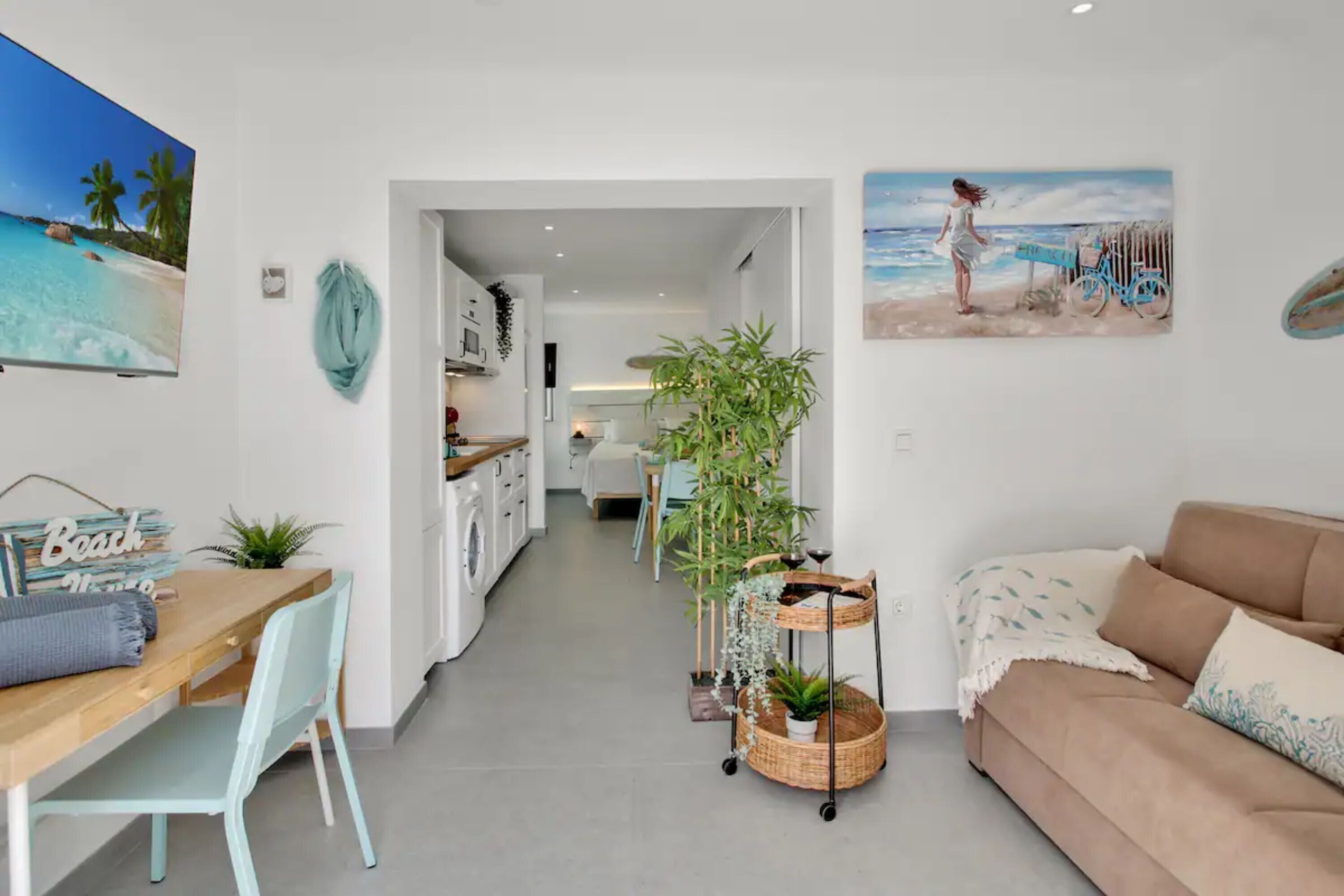 Un salon moderne avec un canapé, un coin repas avec une table et des chaises, une cuisine à l’arrière-plan et un couloir menant à une autre pièce.