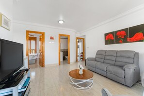 A living room with a grey sofa, a TV, a coffee table, and a painting of red flowers.