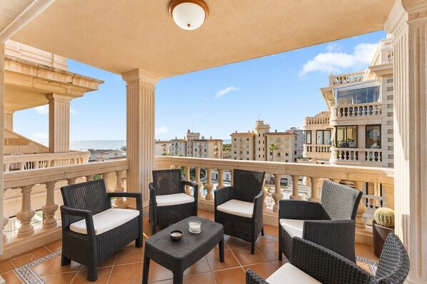 A balcony with wicker furniture, a table with a candle, and a view of the cityscape. - Apartment 'Penthouse, Zeezicht Guardamar' with Sea View, Wi-Fi and Air Conditioning (Guardamar)