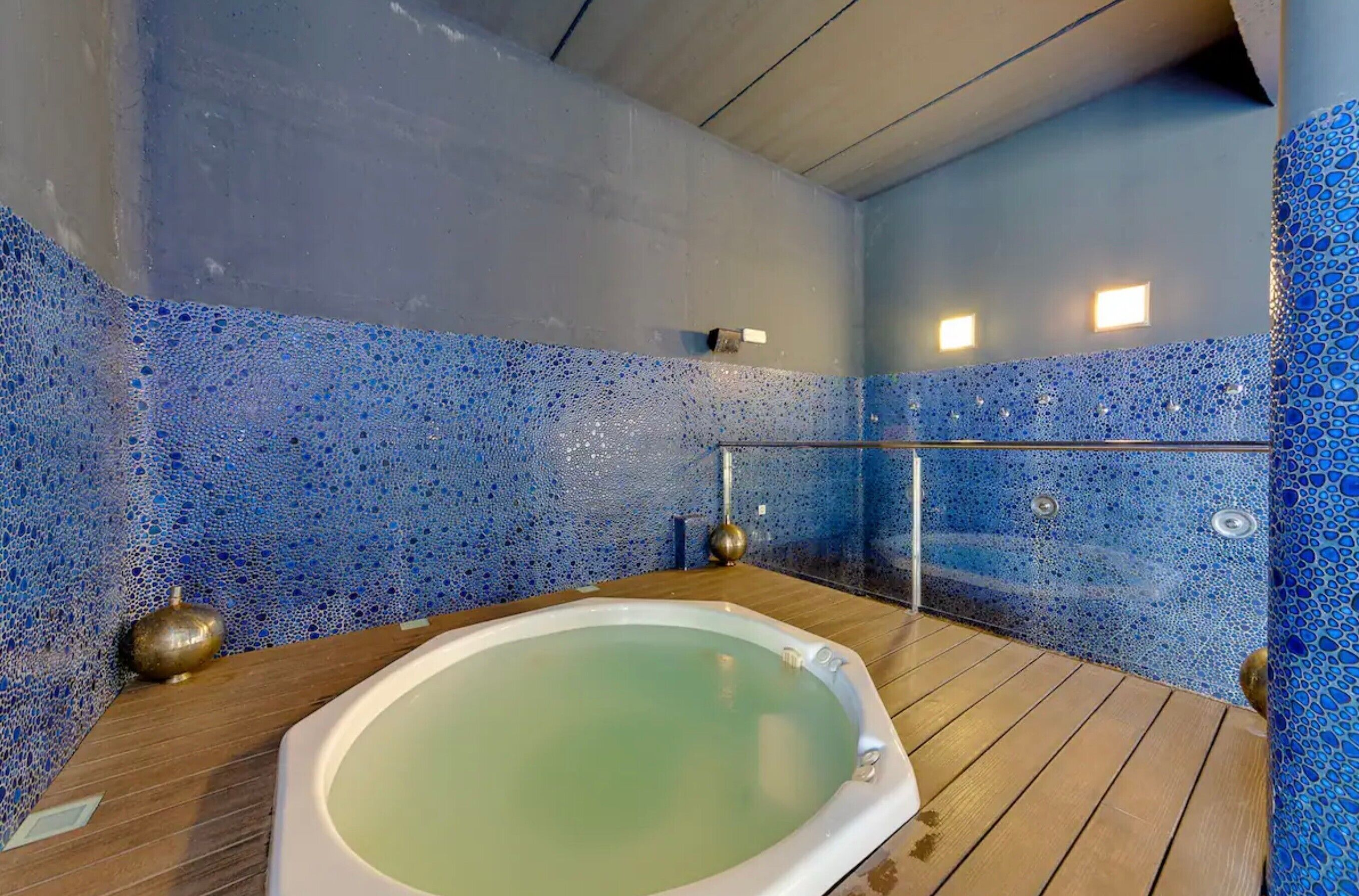 Un cuarto de spa con suelo de madera, una bañera grande y paredes de mosaico azul.