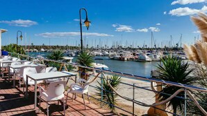 A marina with boats, a dining area with tables and chairs, and a clear blue sky.