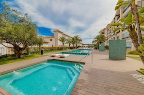 A swimming pool area with a wooden deck, palm trees, and a building with balconies. - Apartment 'Guardamar Hill Resort Spa' with Sea View, Wi-Fi and Air Conditioning (Guardamar)