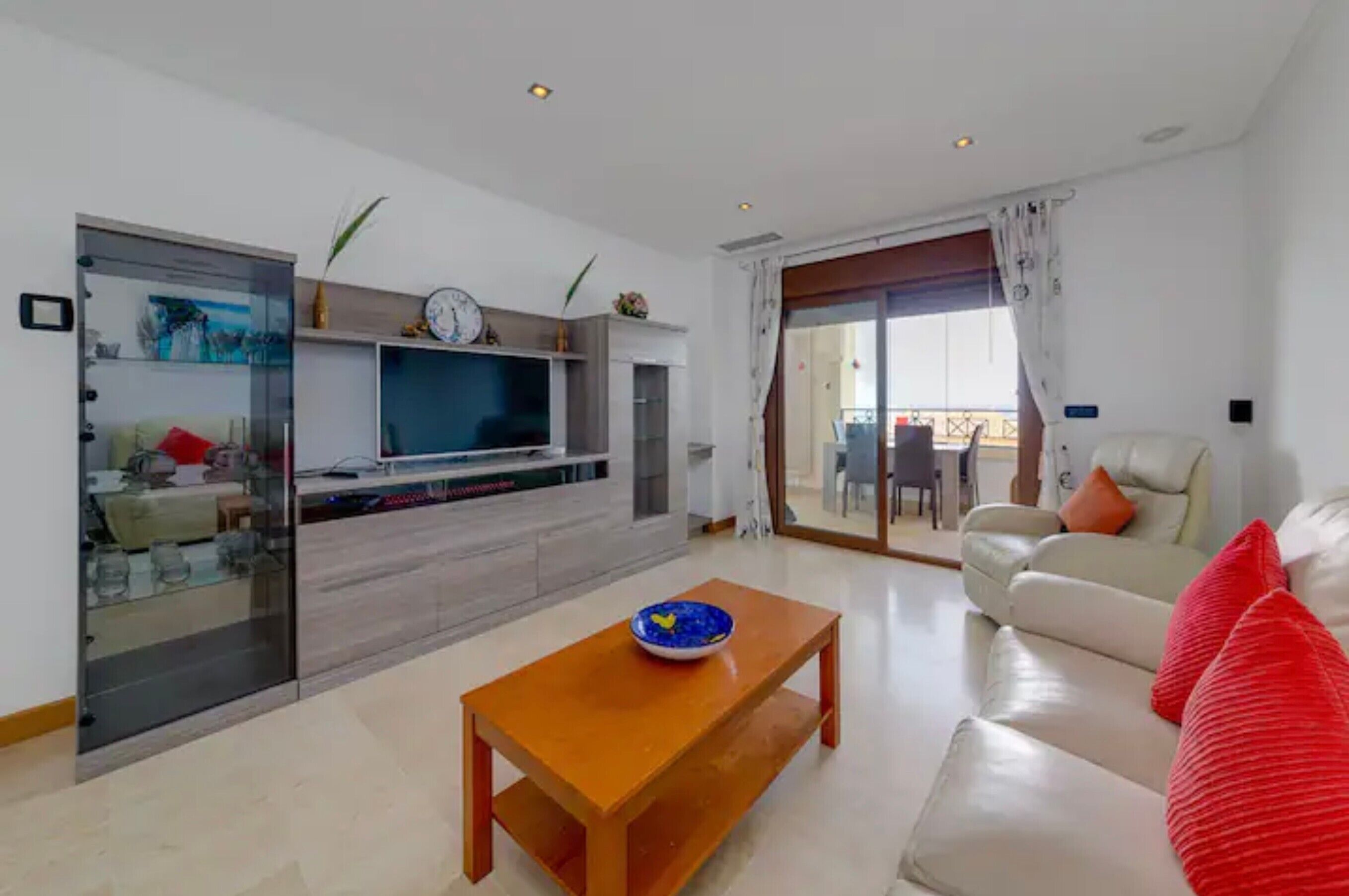 Una sala de estar moderna con un sofá, una mesa de centro de madera, un televisor y un gran ventanal corredizo que da a un balcón.