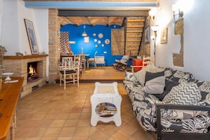 A cozy living room with a fireplace, a patterned sofa, a small white table, and a blue wall with decorative plates.