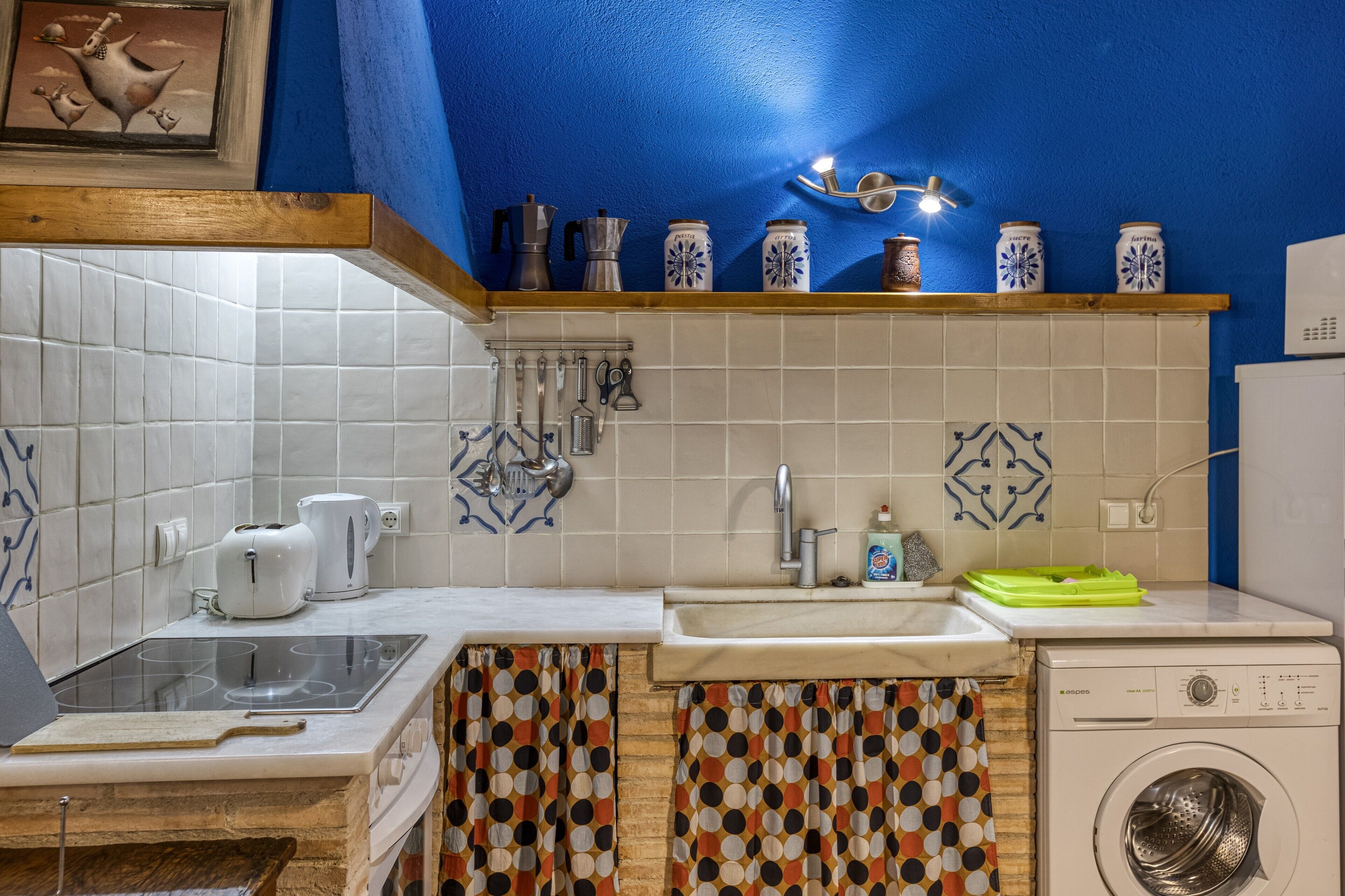 Una cocina con azulejos blancos, un lavamanos, una estufa, una lavadora y una pared azul.