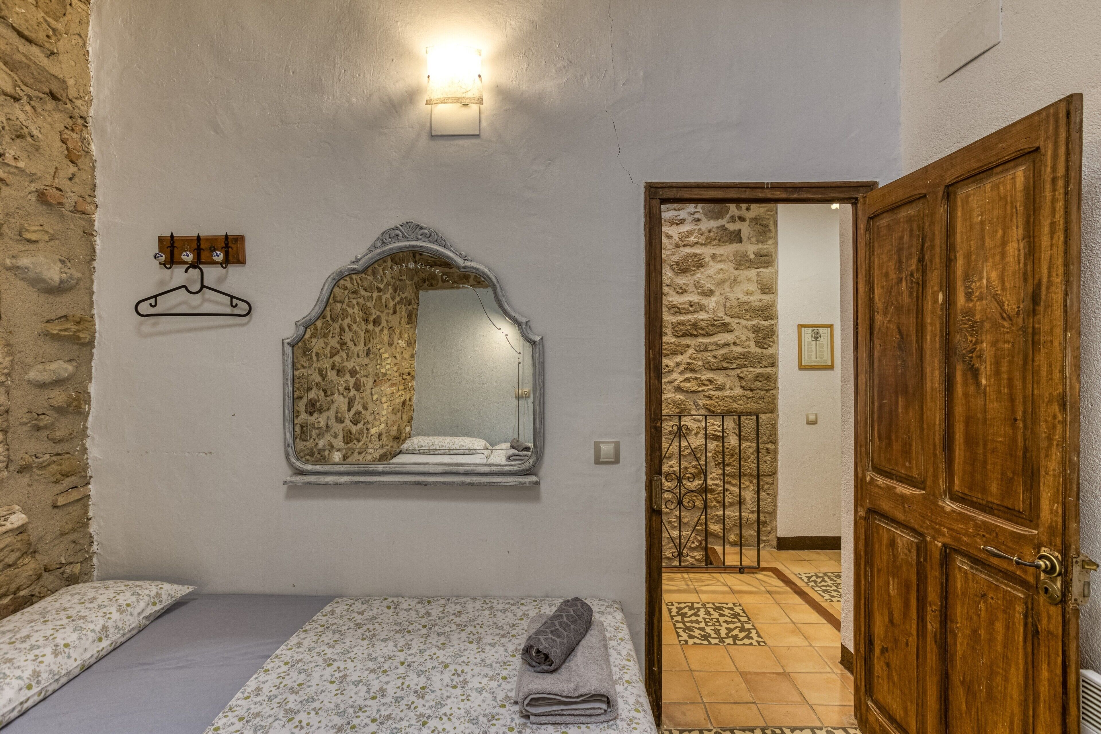 A bedroom with a bed, a hanging coat rack, a mirror, and a wooden door.