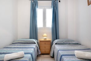 Ein Schlafzimmer mit zwei Betten, einem Nachttisch mit Lampe und einem Fenster mit Vorhängen.