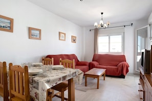 Ein Essbereich mit Tisch für vier Personen, einer roten Couch, einem Fernseher und einer Chandelüster.