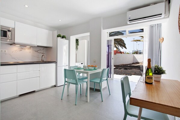 Une cuisine moderne avec des meubles blancs, un pare-feu en marbre et un coin repas doté de chaises turquoise et d’une table en bois.