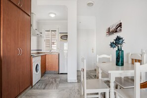 A kitchen with wooden cabinets, a washing machine, a refrigerator, and a dining area with a table and chairs. - Apartment 'Casa Miren' with Balcony, Wi-Fi and Air Conditioning (Conil de la Frontera)