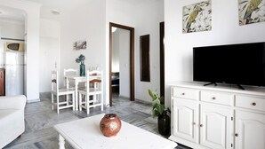 Una sala de estar moderna con un sofá blanco, una mesa de comedor y un televisor sobre un mueble blanco.