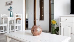 Una mesa blanca con un farol de cobre, una silla blanca, un armario blanco y un girasol al fondo.
