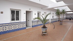Un pasillo con paredes blancas, baldosas con diseño azul y beige, y plantas en macetas.