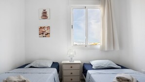 Un dormitorio con dos camas, una mesita de noche, una lámpara y una ventana con cortinas.