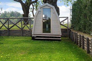Une petite construction en bois dotée d’une porte, entourée d’une clôture en bois et d’arbres.