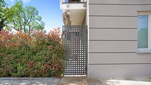 A paved walkway leading to a building with a metal gate, a hedge, and a clear sky.
