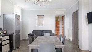 A modern kitchen with a dining table, chairs, a refrigerator, and a flat-screen TV.