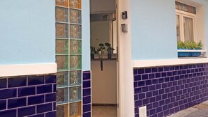 A building entrance with a glass door, a window with plants, and a tiled wall.