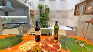 A kitchen with a wooden table set for a meal, featuring a bottle of wine, cheese, olives, and cured meats.