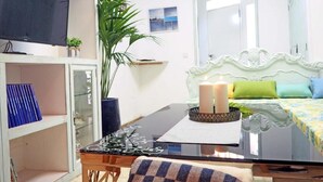 A room with a bed, a television, a dining table, and a plant.