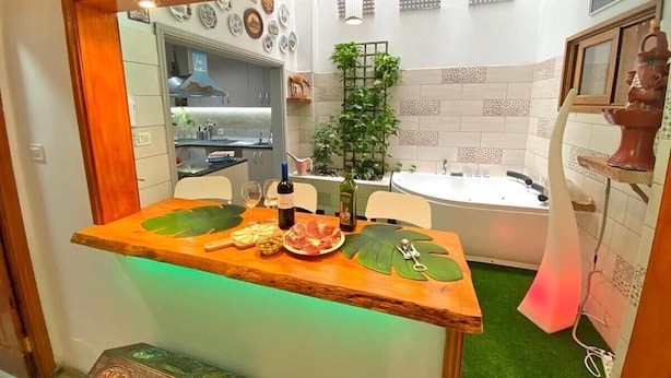 A kitchen with a wooden bar counter, a dining table, a sink, and a bathtub.
