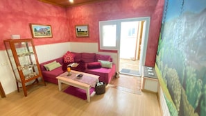 A room with a pink sofa, a small table, a glass cabinet with items, and a door leading outside.