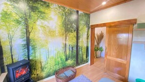 A room with a large forest mural, a fireplace, a wicker sofa, and a wooden door. - Vacation Home 'Las Vistas' with Mountain View, Private Terrace and Wi-Fi (Valleseco)