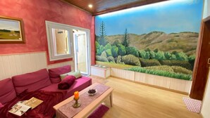 A room with a red couch, a wooden table with a candle, and a mural of a landscape. - Vacation Home 'Las Vistas' with Mountain View, Private Terrace and Wi-Fi (Valleseco)