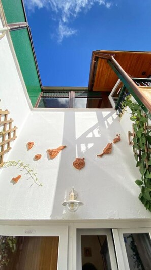 A white exterior wall with a wooden staircase, a metal railing, and a small light fixture.
