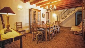 Un comedor con una mesa y sillas de madera, una araña, una escalera y un aparador con puertas de cristal.