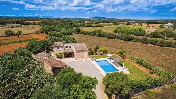 Una casa de piedra con piscina, rodeada de vegetación y campos.