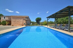 A swimming pool with lounge chairs, a stone building, and a covered area.
