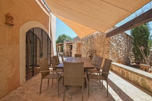 An outdoor patio with a round table and wicker chairs, a stone wall, and a metal gate.