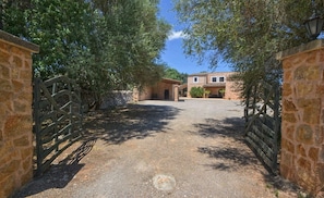 A gravel driveway leading to a stone building with a gated entrance, surrounded by trees.