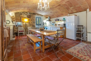 Una cocina rústica con pared de piedra, mesa de madera, banco y una araña.