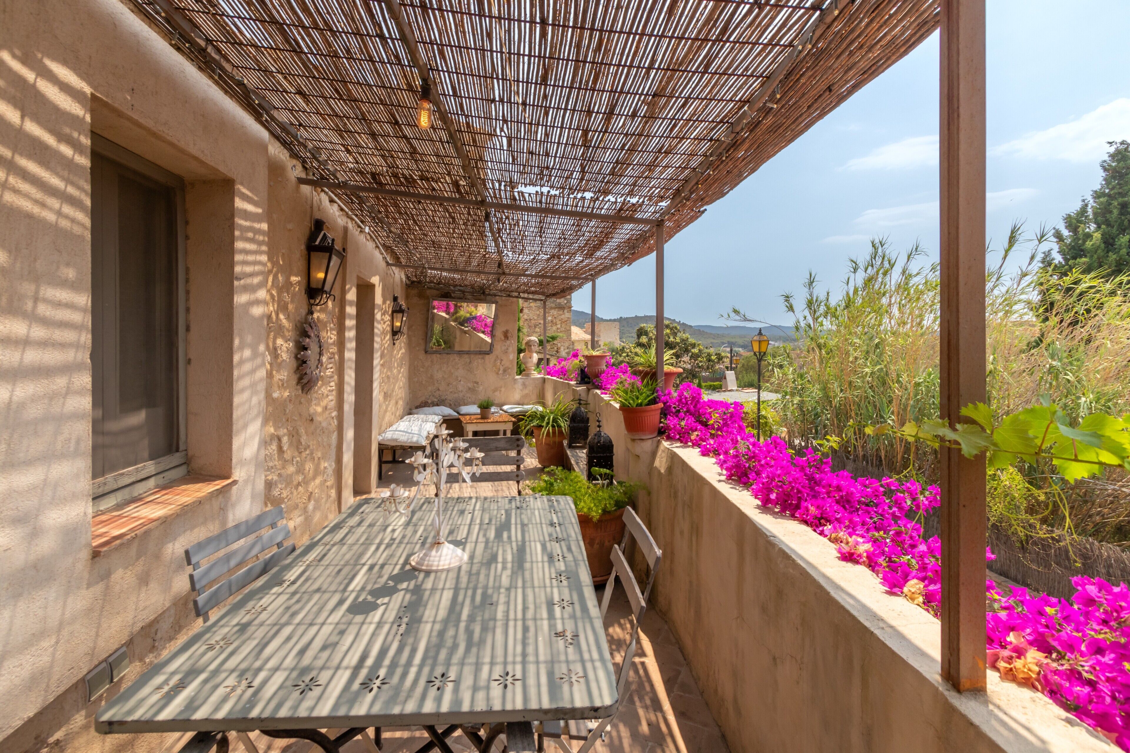 A covered outdoor patio with a table and chairs, potted plants, and a view of the surrounding landscape.