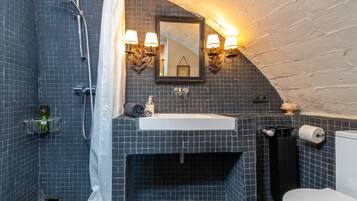 Un baño con ducha, lavamanos, inodoro y espejo con apliques de pared.