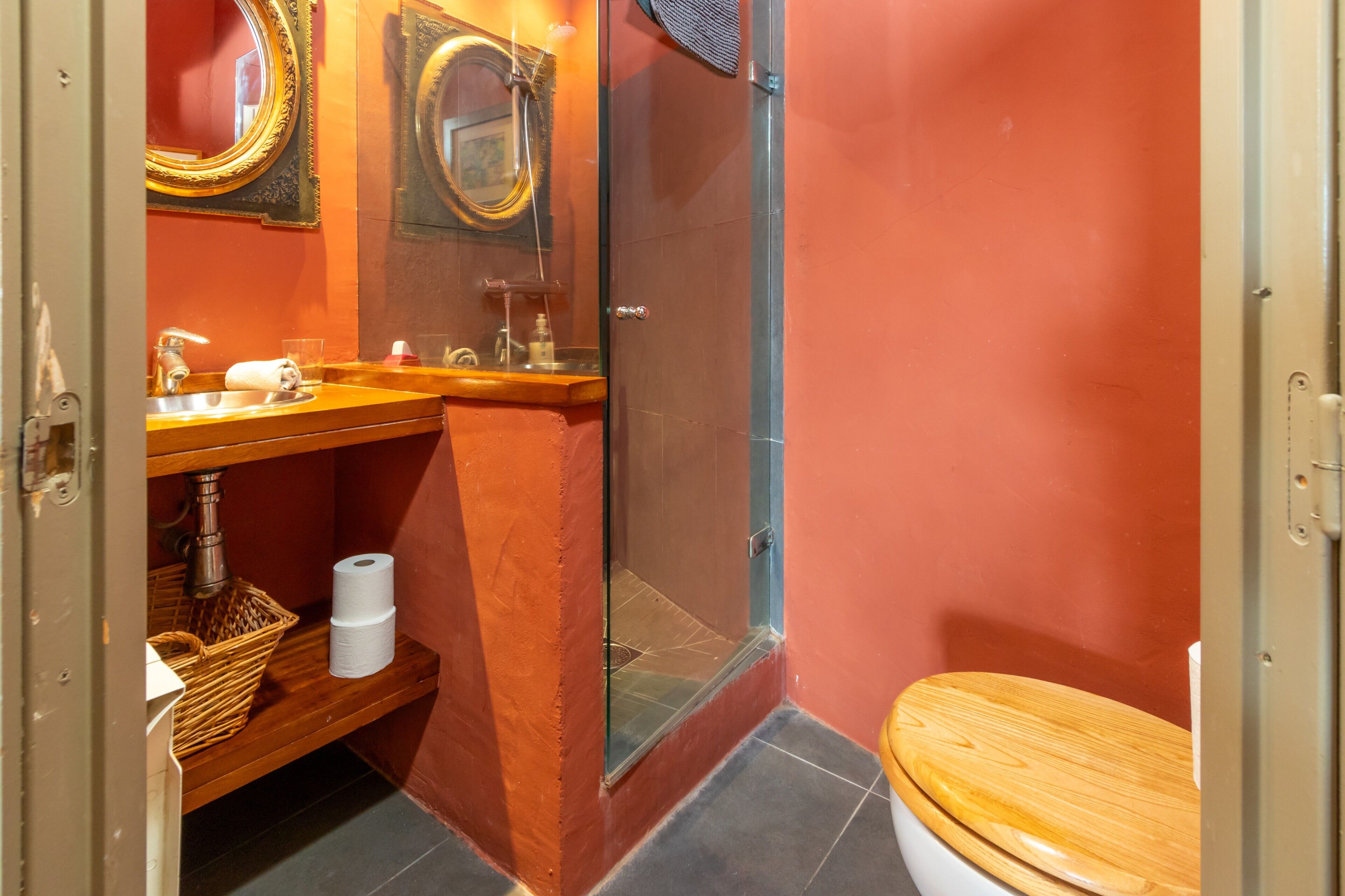 A bathroom with a wooden vanity, a glass shower enclosure, a toilet, and a mirror with an ornate frame.