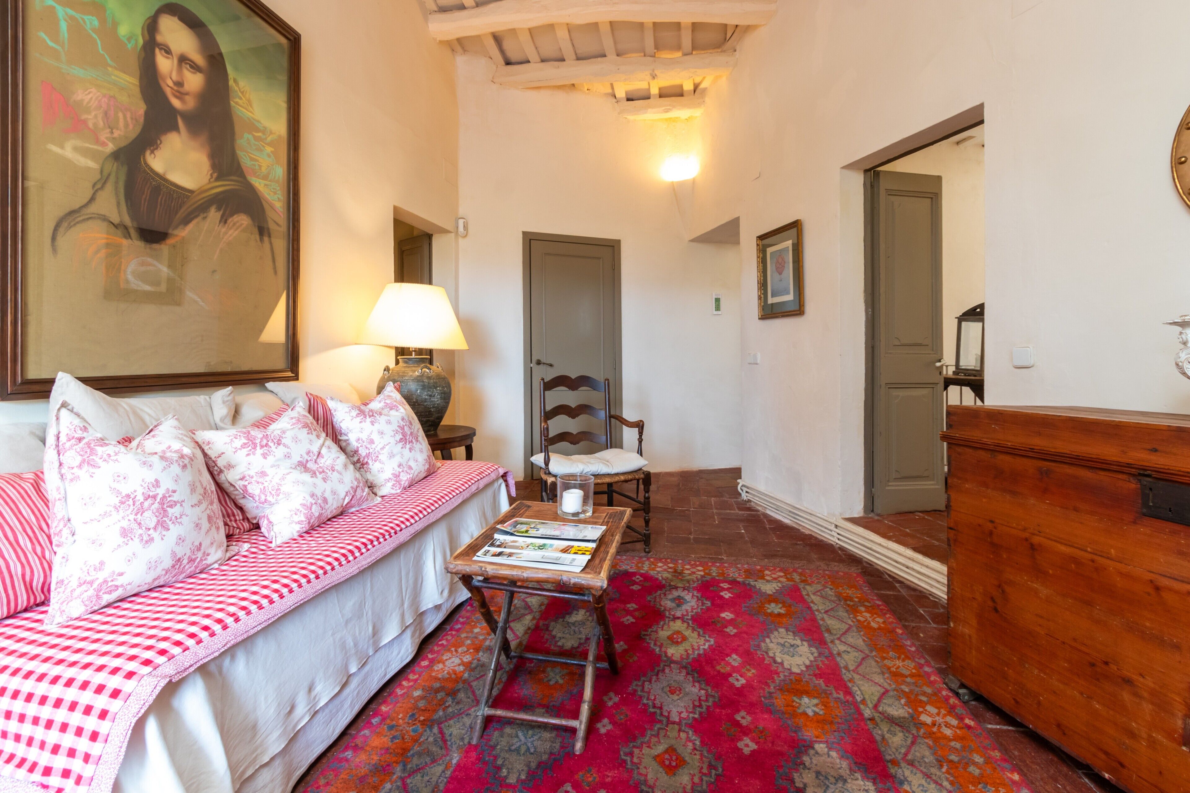 Une pièce chaleureuse avec un canapé, un fauteuil, une commode en bois, une lampe et une œuvre d’art encadrée accrochée au mur.