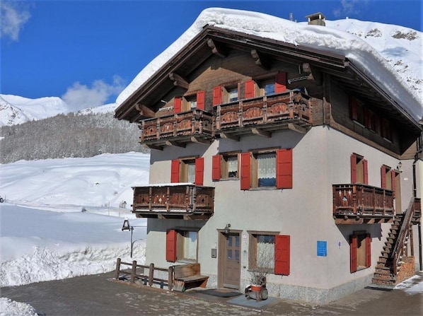 A multi-story building with balconies, a wooden staircase, and a snow-covered landscape.