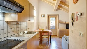 A kitchen with a stove, sink, and wooden cabinets. There is a dining table with chairs and a small window. - Apartment 'Appartamenti Lorenza 3 Baite Giotto' with Mountain View, Shared Garden and Wi-Fi (Livigno)
