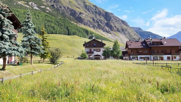 A mountain lodge with a wooden exterior, a covered porch, and a view of the surrounding hills. - Apartment 'Appartamenti Lorenza 3 Baite Giotto' with Mountain View, Shared Garden and Wi-Fi (Livigno)