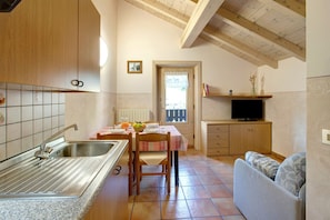 A kitchen with a sink, a dining table with chairs, a television on a stand, and a sofa.