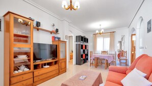 Un salon équipé d’un téléviseur, d’un meuble en bois, d’un canapé orange et d’un coin repas avec une table et des chaises.