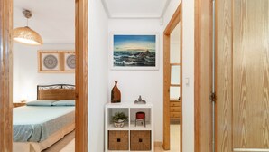 A bedroom with a bed, a bedside table with a lamp, a wall-mounted painting, and a wooden door. - Holiday Home 'casa en la playa con piscina y terraza MAX' (Gran Alacant)