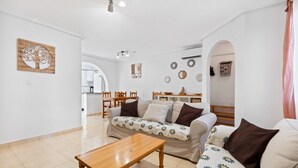 A living room with a sofa, a wooden coffee table, and a dining area with chairs and a table. - Holiday Home 'casa en la playa con piscina y terraza MAX' (Gran Alacant)
